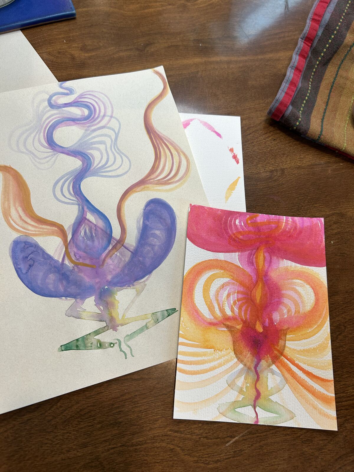 Two watercolor studies -- a blue-purple winged energy form and a radiating pink-orange winged energy form
